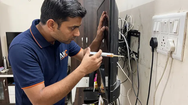 AHC technician applying cockroach gel bait behind a wall-mounted TV