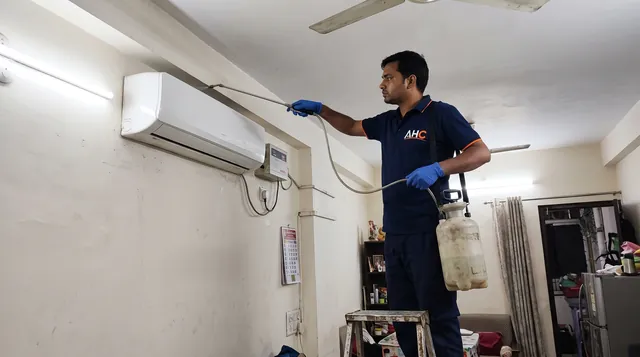AHC technician on a step ladder spraying behind a wall-mounted AC for lizard control